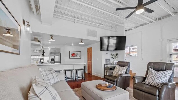 A spacious living area with a sofa, armchairs, a coffee table, a kitchen in the background, and a ceiling fan. - Dickson St. Hideaway (Fayetteville)