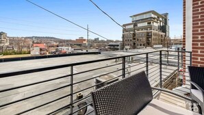 A rooftop terrace with a metal railing, a view of the cityscape, and a building with multiple floors. - Dickson St. Hideaway (Fayetteville)