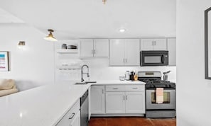 Une cuisine moderne avec des meubles blancs, un micro-ondes noir, une cuisinière et un évier.