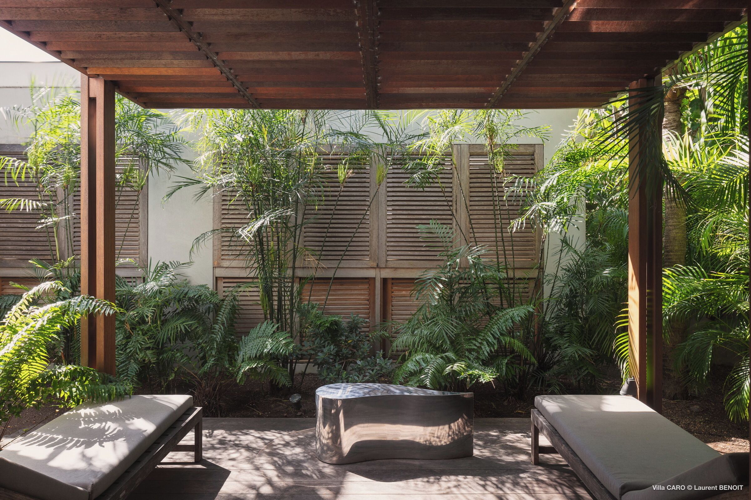 Un espacio de estar al aire libre techado, con dos sillones cómodos y una mesa central, rodeado de exuberante follaje tropical.