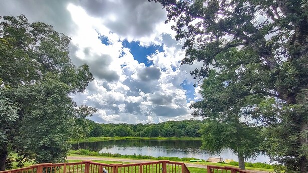 Una terraza de madera con mobiliario exterior con vistas a un lago y zona boscosa.