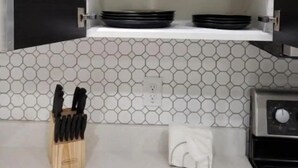 Una cocina con encimeras blancas, salpicadero de azulejos hexagonales y electrodomésticos negros.