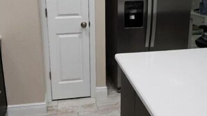A kitchen with a white door, stainless steel refrigerator, and a white countertop. - Tropical Pardise A (Tampa)