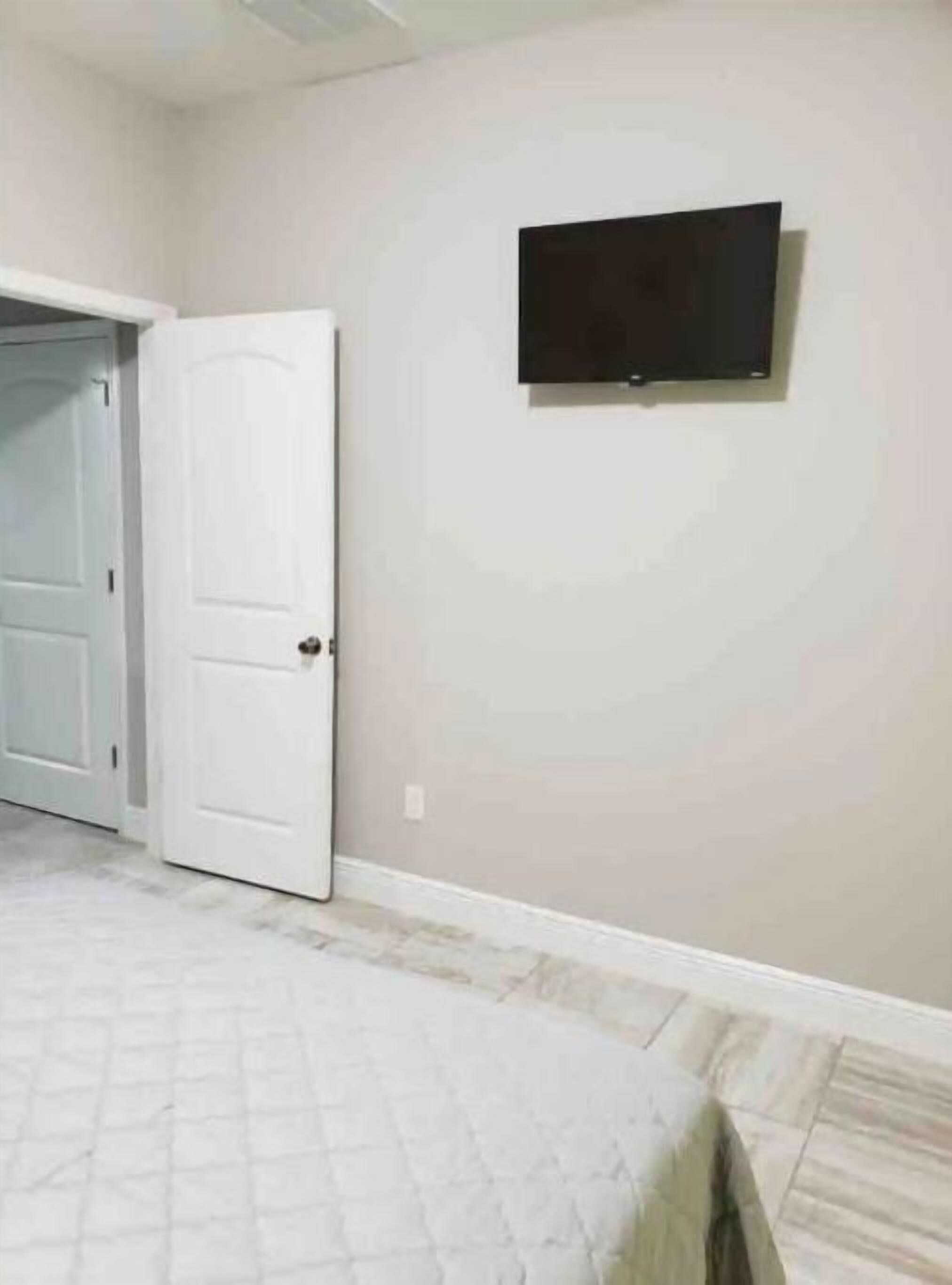 A bedroom with a bed, a door, and a television mounted on the wall.