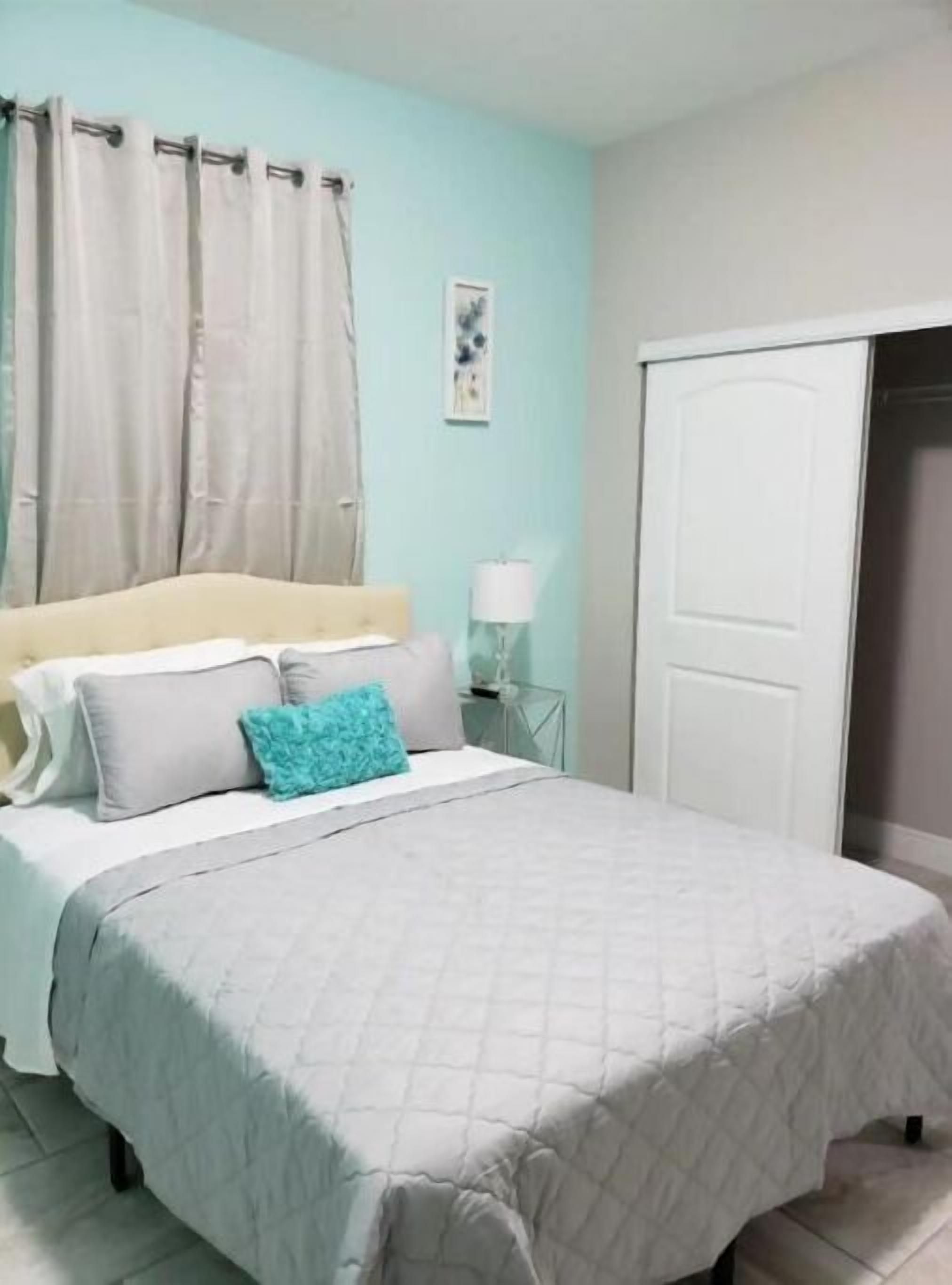 A bedroom with a bed, curtains, a bedside lamp, and a door.