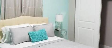 A bedroom with a bed, curtains, a bedside lamp, and a door.