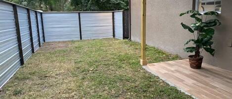 A backyard with a metal fence, a wooden deck, and a potted plant.