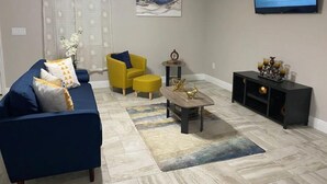 A living room with a blue sofa, yellow armchair, and a coffee table. A flat-screen TV is mounted on the wall, and there is a small side table with decorative items. - Tropical Pardise A (Tampa)