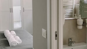 A hotel room with a bed, a bathroom with a sink and mirror, and a towel on the bed. - Standard double room (Roma)