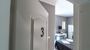 A hallway with a door marked '3' leading to a bedroom with a bed, a desk, and a mirror. - Standard double room (Roma)