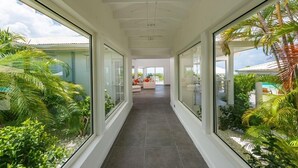 Ein modernes Interieur mit einer Glaskonstruktion, die zu einem Wohnbereich führt, umgeben von üppiger Vegetation.