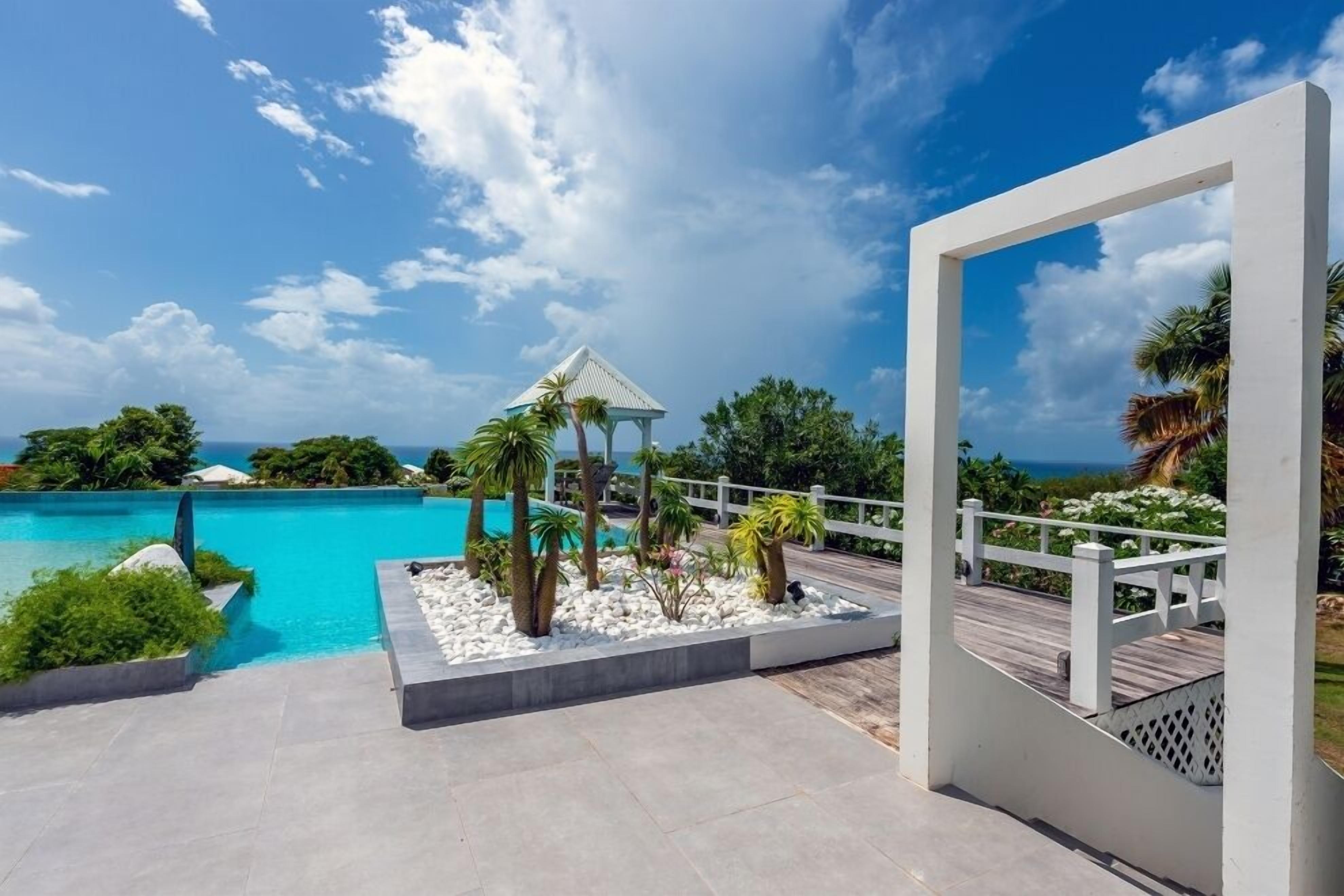 A resort pool area with a gazebo, palm trees, and a wooden deck overlooking the ocean.