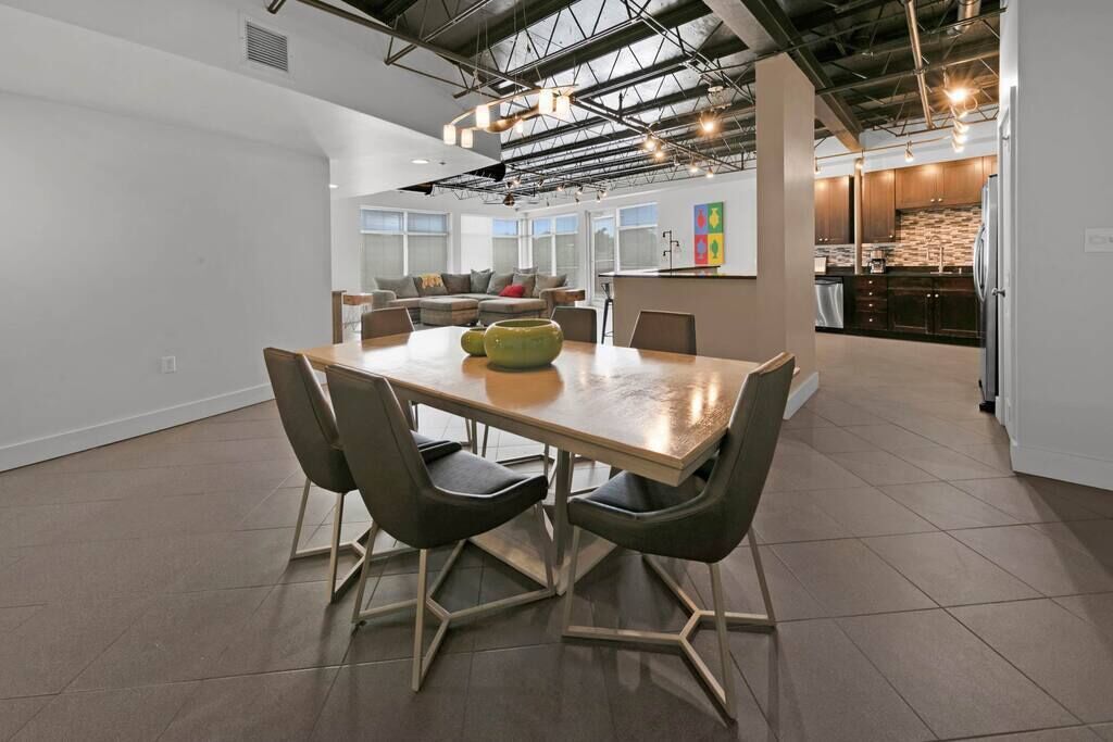 A modern kitchen with dark cabinets, a central island, and a dining area with a wooden table and chairs.