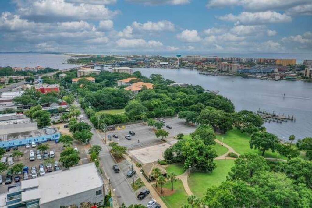 Un paisaje urbano costero con un puerto deportivo, zonas verdes de parque y una mezcla de edificios residenciales y comerciales.
