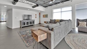 Un salon moderne avec un canapé d’angle gris, une table basse en bois et un grand tapis.