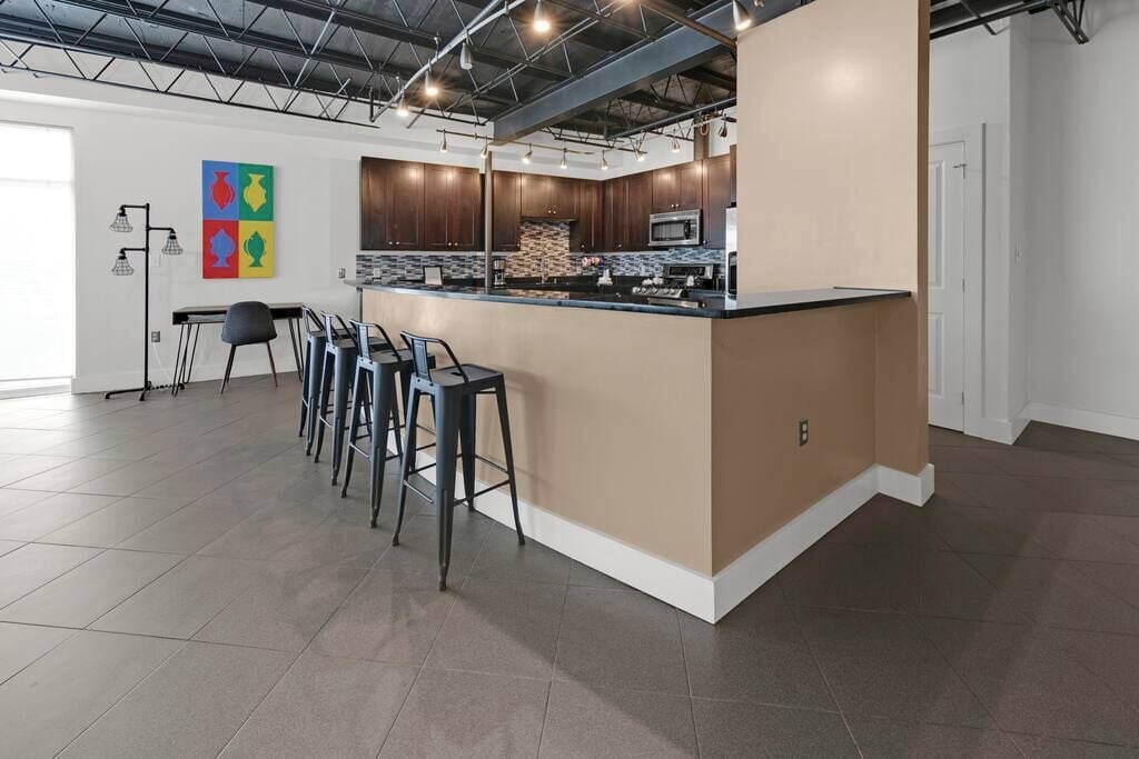 A modern kitchen with a central island, bar stools, and a colorful artwork on the wall.