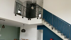Un amplio salón con mesa de comedor, sillas, sofá, escalera y ventilador de techo.