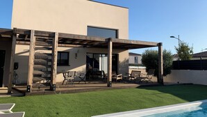 Una casa moderna con un porche cubierto, mobiliario de exterior y una piscina.