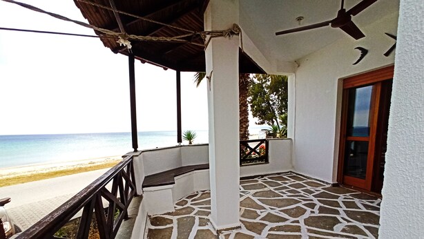 A covered outdoor area with a stone floor, a wooden bench, and a view of the beach. - Zennova 22 Nikiti Sea Side House (Sithonia)