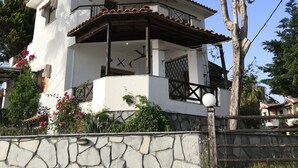 A white building with a tiled roof, a balcony with a railing, and a stone wall in front. - Zennova 22 Nikiti Sea Side House (Sithonia)