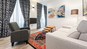 Ein modernes Wohnzimmer mit einem grauen Sofa, einem grauen Sessel, einem Teppich mit roten und schwarzen Mustern und blumigen, schwarz-weißen Vorhängen.