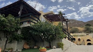 A building with a sloped roof, a stone wall, and a small garden area with potted plants. - Alonaki House (Listaros)