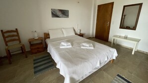 A neatly arranged bedroom with a large bed, a wooden chair, a bedside table with a lamp, a small table with a glass, and a mirror on the wall. - Alonaki House (Listaros)