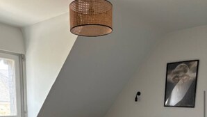 A bedroom with a sloped ceiling, a bed with patterned bedding, a wall-mounted lamp, and a framed picture. - Apartment 20 minutes from the beaches (BRECH)