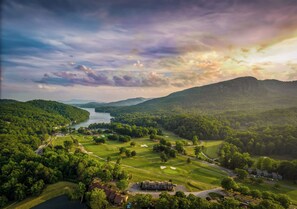Un parcours de golf avec un lac, entouré de collines boisées et d’une montagne qui se profile à l’horizon.