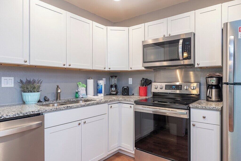 A modern kitchen with white cabinets, stainless steel appliances, and a granite countertop.