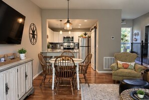Une cuisine moderne avec un coin repas, un téléviseur à écran plat fixé au mur et un coin salon confortable avec un fauteuil à motifs et un pouf.