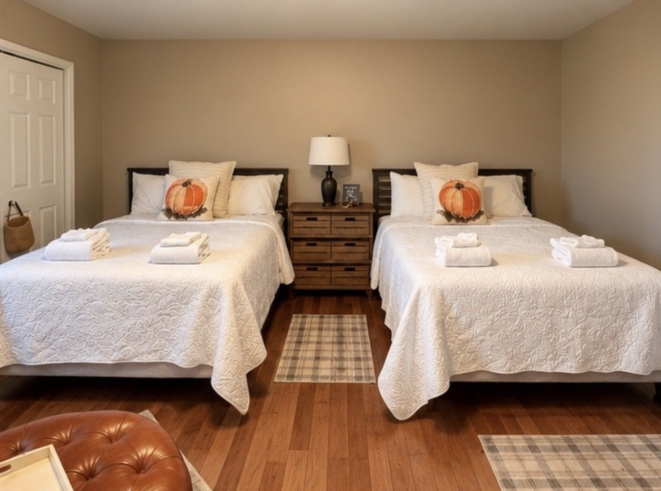 A hotel room with two beds, a wooden floor, a plaid rug, and a brown leather chair.