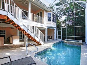 Una casa de dos pisos con piscina, un patio cubierto y una escalera con iluminación exterior.