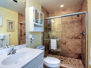 Un baño con lavamanos blanco, inodoro, cabina de ducha con mampara de vidrio y espejo.