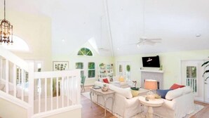 Ein helles Wohnzimmer mit weißer Wendeltreppe, einem an der Wand montierten Fernseher und einem Deckenventilator.