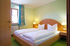 A double bed with white linens, two bedside tables with lamps, a window with curtains, and a radiator.
