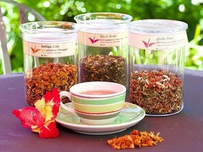 Three glass containers with herbal tea labels, a striped cup, and a flower on a table.