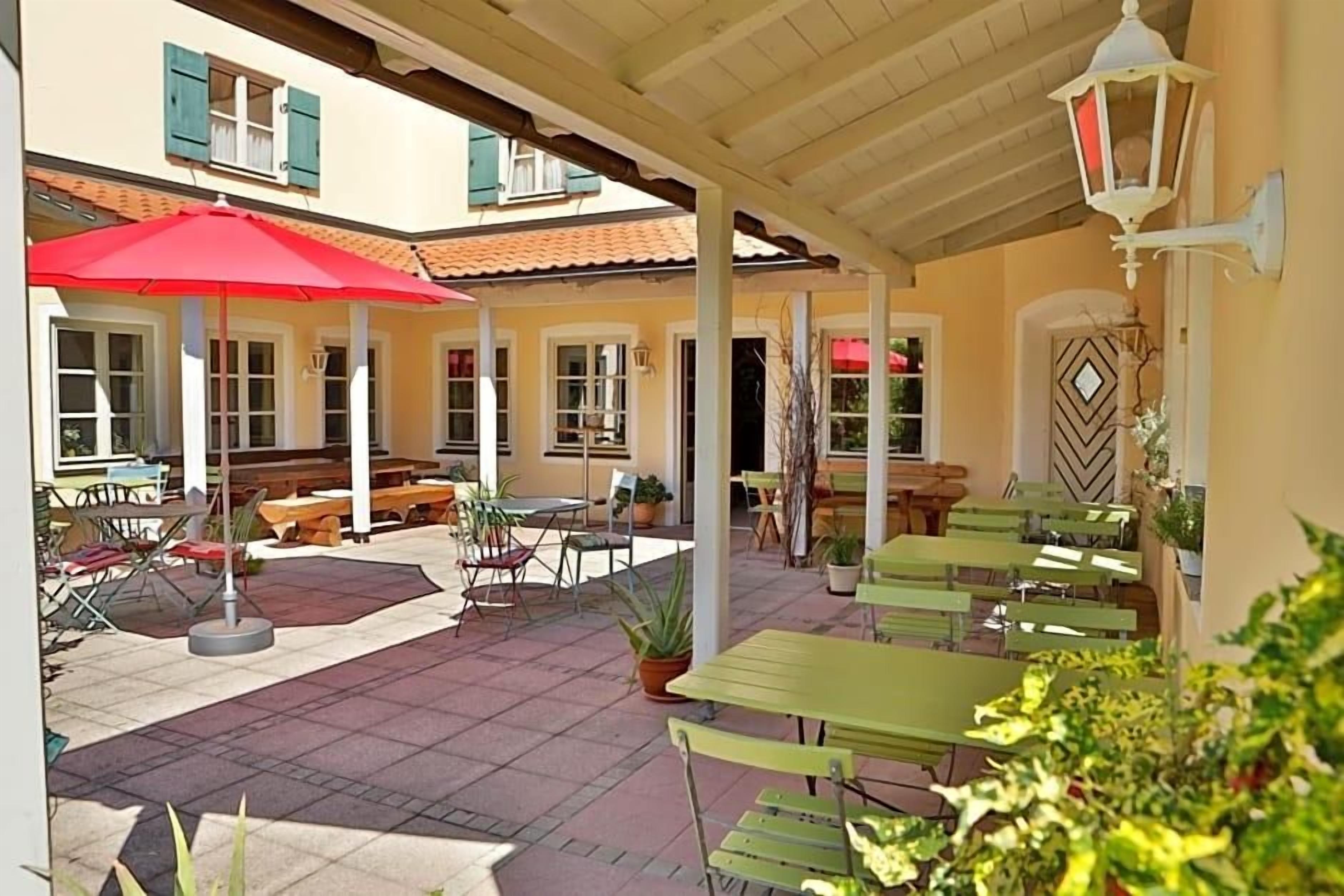 An outdoor patio area with tables and chairs, a red umbrella, and potted plants.