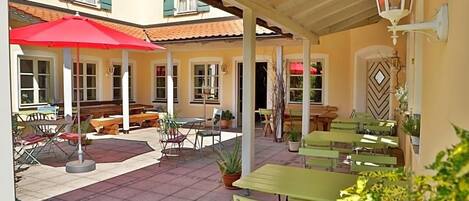 An outdoor patio area with tables and chairs, a red umbrella, and potted plants.
