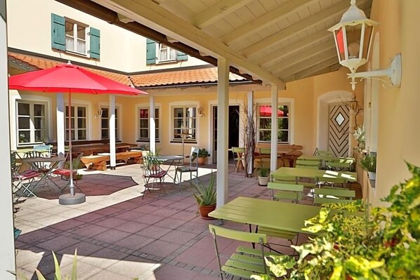 An outdoor patio area with tables and chairs, a red umbrella, and potted plants.