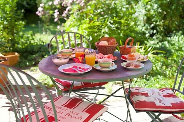A round metal table with a picnic setup including plates, cups, and a basket.