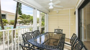 A glass-top table with chairs on a balcony with a view of a swimming pool and palm trees. - Villa Sanibel 2B (Sanibel)