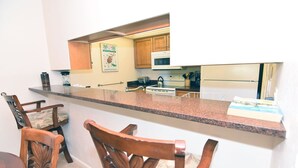 A kitchen with a granite countertop, wooden chairs, a microwave, and a refrigerator. - Villa Sanibel 2B (Sanibel)