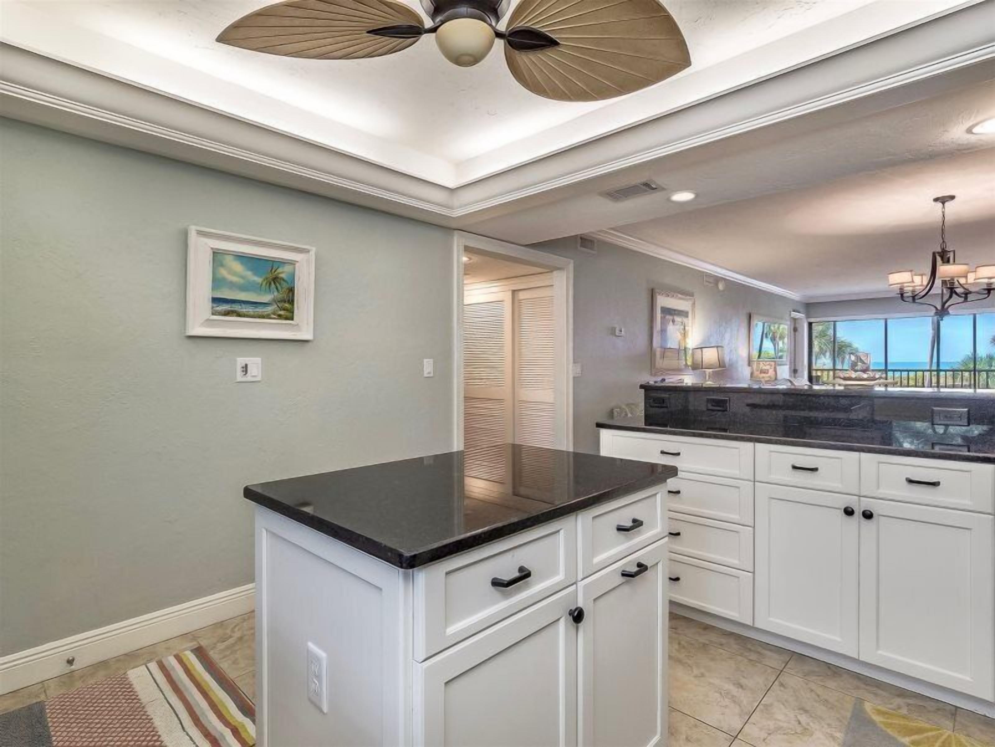 A kitchen with white cabinets, a black countertop, and a ceiling fan.
