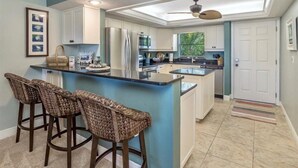 Une cuisine moderne dotée d’un îlot central, de tabourets de bar et d’un ventilateur de plafond.