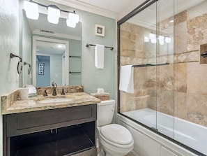 A bathroom with a marble sink, a toilet, and a glass-enclosed shower. - Sand Pointe 212 (Sanibel)