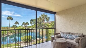 Un balcon avec vue sur une piscine et des palmiers, un canapé en osier et une table ronde en osier.