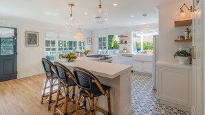 A modern kitchen with a central island, bar stools, pendant lighting, and a view to the outside. - Casa Miramar - Coastal Farmhouse Chic Getaway (Santa Barbara)