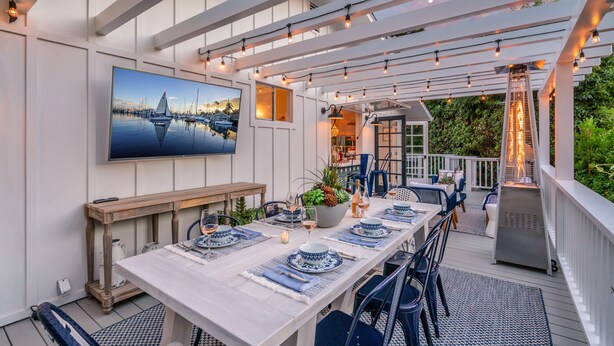 A covered outdoor dining area with a long table set for six, surrounded by blue chairs. - Casa Miramar - Coastal Farmhouse Chic Getaway (Santa Barbara)