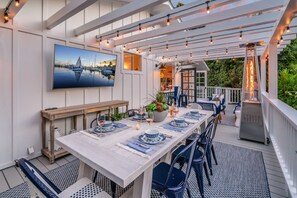 Een overdekt terras met een lange tafel voor zes personen, omringd door blauwe stoelen.